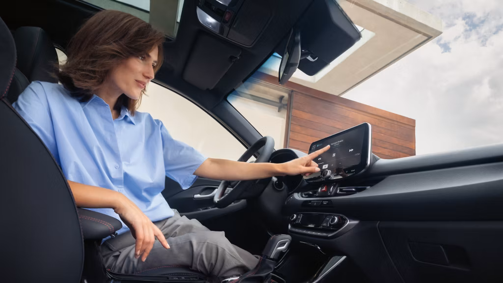 A woman sitting in the driver’s seat, using the multimedia touchscreen on the dashboard.